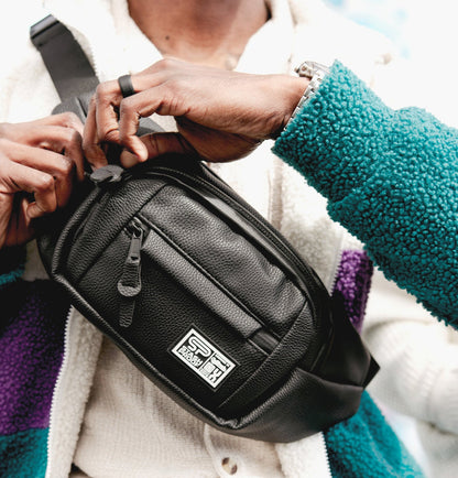 Man holding Transporter leather crossbody and fanny pack to the camera while unzipping top