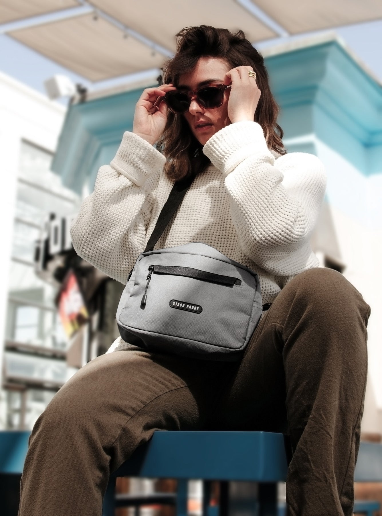 Woman in white sweater and red glasses wearing grey Rover bag while sitting