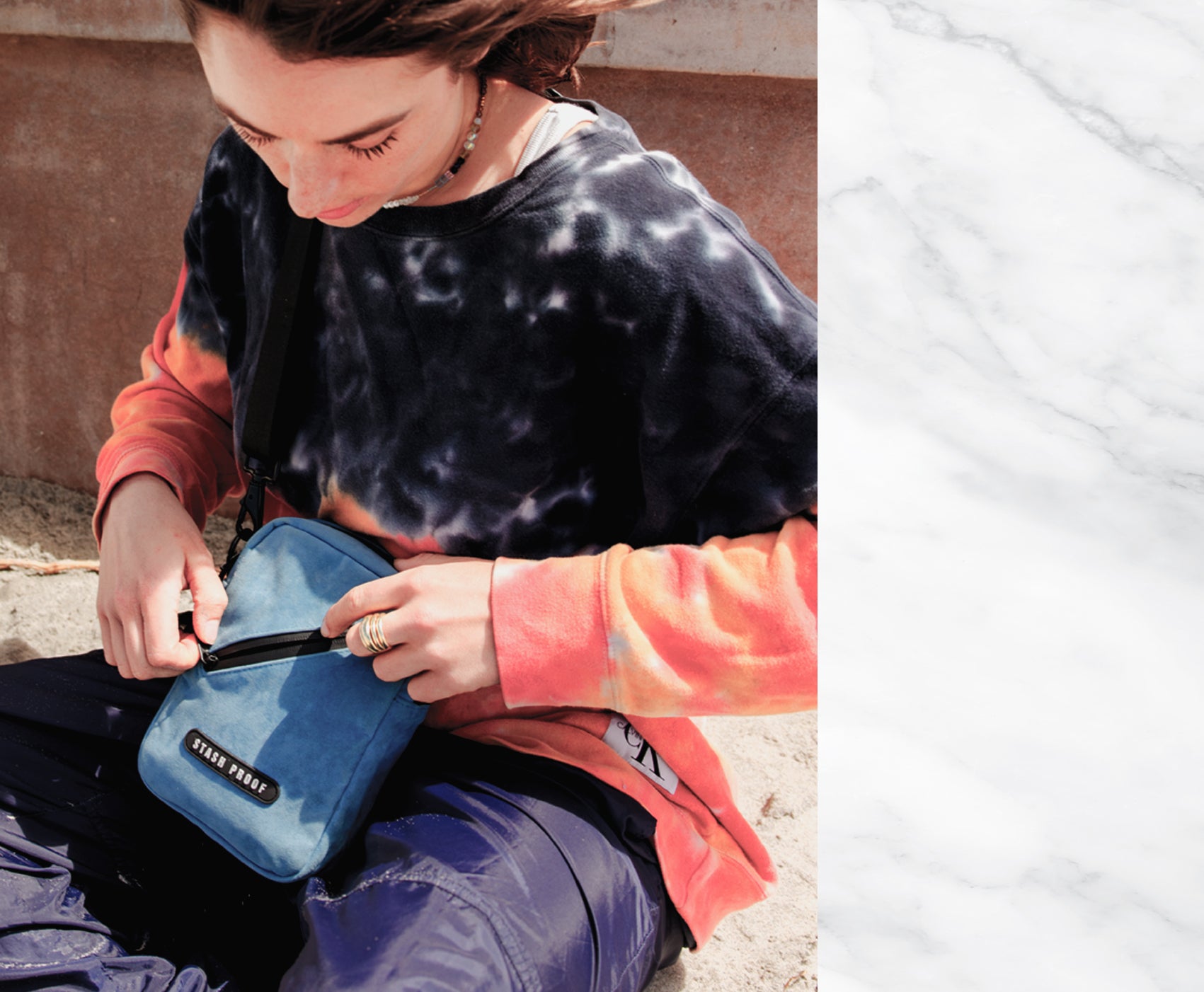 Girl sitting on sand holding a blue Stash Bag by Stash Proof