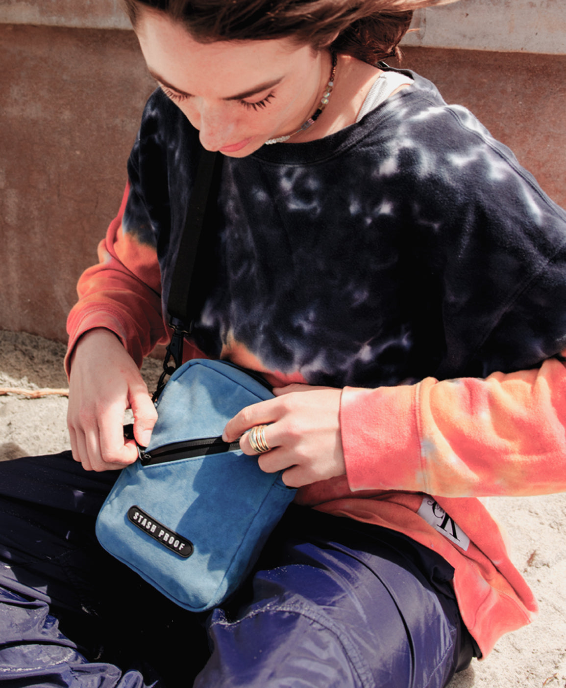 Girl sitting on sand holding a blue Stash Bag by Stash Proof